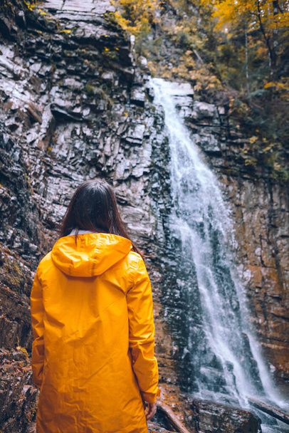 woman in yellow raincoat at autumn waterfall - Photo, Image