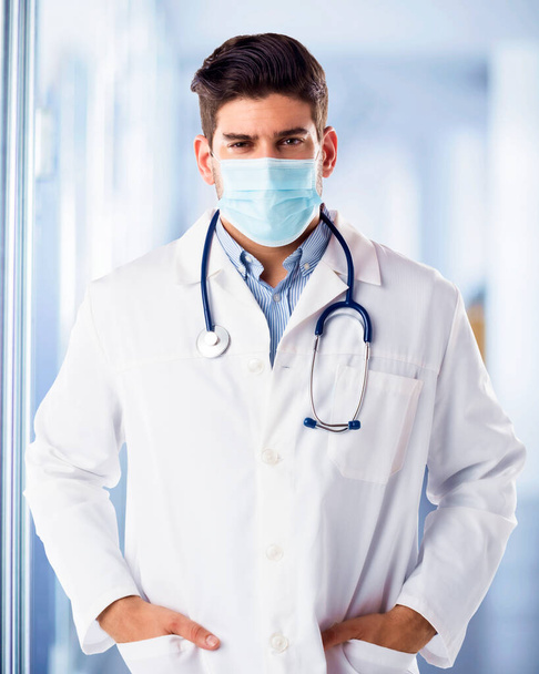 Retrato del médico masculino con mascarilla facial para la prevención mientras está de pie en el vestíbulo de los hospitales - Foto, imagen