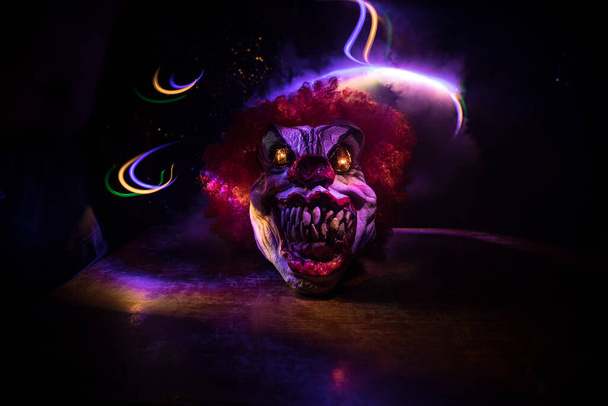 Spookachtige Clown hoofd op houten tafel. Kwade clown glimlachend op donkere mistige achtergrond. Halloween concept. Selectieve focus - Foto, afbeelding