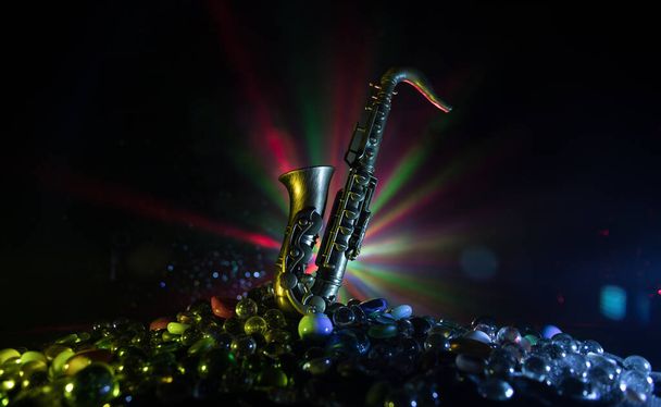 Concept musical. Instrument de jazz saxophone. Alto or sax miniature avec une lumière tonique colorée sur fond brumeux. Instrument de musique saxophone en faible luminosité. Concentration sélective - Photo, image