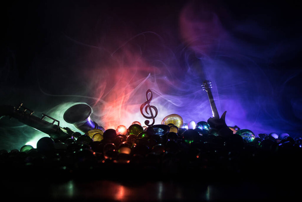 Μουσική έννοια. Μουσικό σύμβολο treble clef από ανοξείδωτο χάλυβα μινιατούρα με πολύχρωμο τονισμένο φως σε ομιχλώδες φόντο. Μουσικά όργανα σε χαμηλό φωτισμό. Επιλεκτική εστίαση - Φωτογραφία, εικόνα