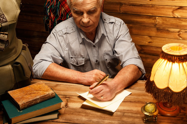Carta de escrita sênior com caneta pena em interior de madeira caseira
  - Foto, Imagem