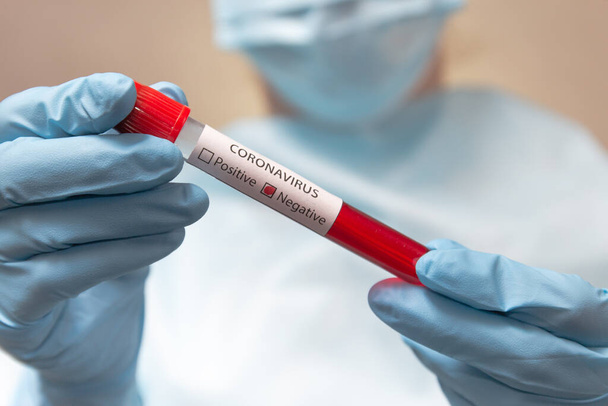 Coronavirus negatif kan testi. Koruyucu giysili doktor, tıbbi maske ve lateks eldivenler içinde kan olan bir tüp tutuyor.. - Fotoğraf, Görsel