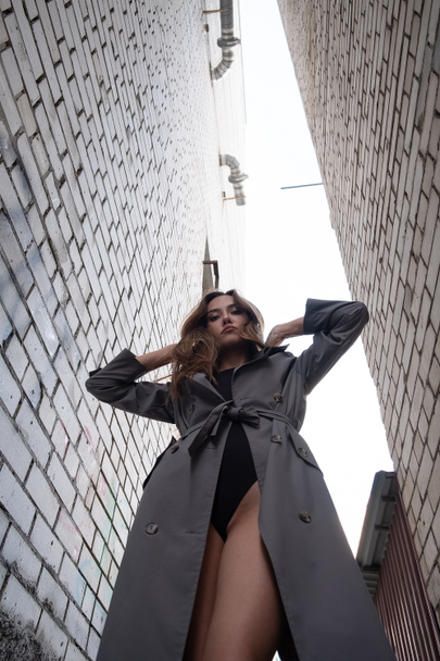attractive asian model in trench coat standing near walls shot from lower point - Photo, Image