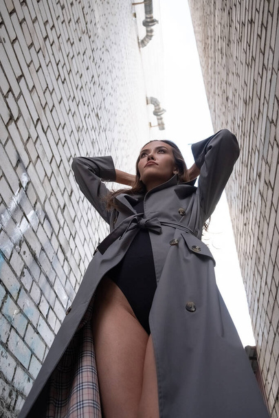 Trençkotlu çekici Asyalı model alt noktadan çekilen duvarların yanında duruyor. - Fotoğraf, Görsel