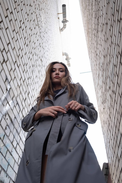 attractive asian model in trench coat standing near walls shot from lower point - Fotoğraf, Görsel