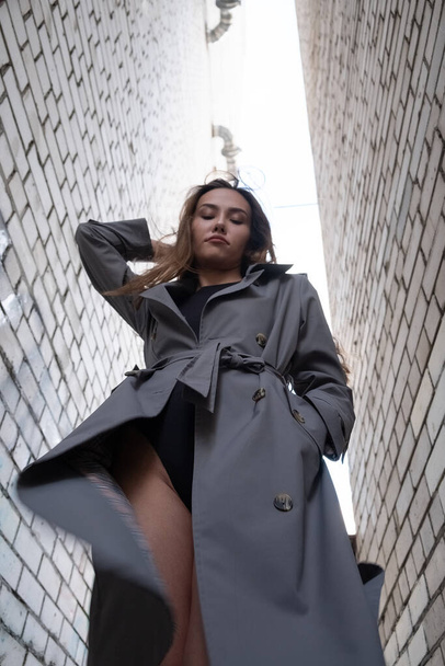 attractive asian model in trench coat standing near walls shot from lower point - Fotografie, Obrázek