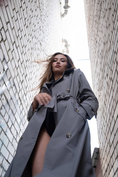 attractive asian model in trench coat standing near walls shot from lower point - Photo, Image