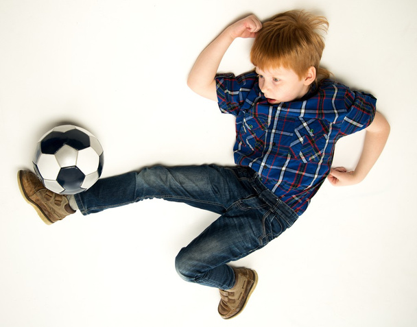 Маленький забавный рыжий мальчик пинает футбольный мяч
 - Фото, изображение