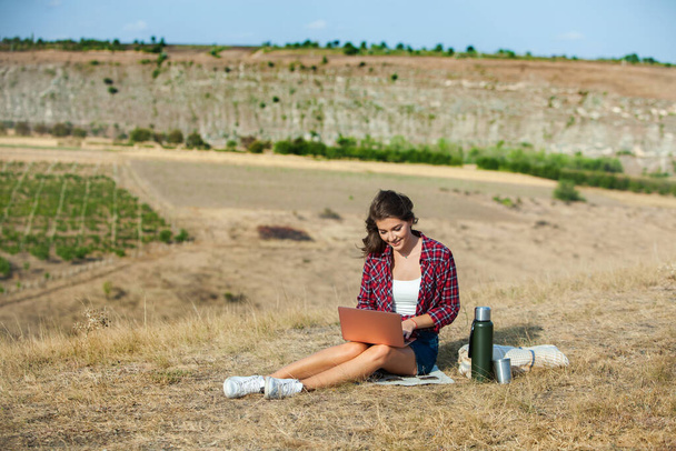 Office outdoors. Beautiful girl works on a laptop in the open air. woman freelancer. Freelance worker concept. - 写真・画像