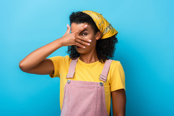 Mujer afroamericana cubriendo el ojo con la mano en azul - Foto, imagen