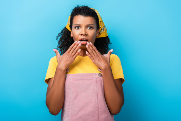 schockierte afrikanisch-amerikanische Frau bedeckt Mund mit den Händen auf blau - Foto, Bild
