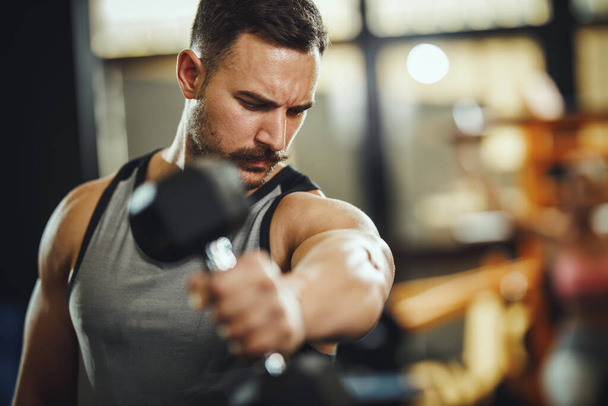 クロストレーニングジムでダンベルと仕事をするスポーツウェアの筋肉の男のショット。彼は体重の重い肩の筋肉を汲み上げている. - 写真・画像