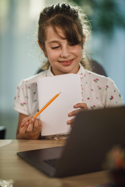 Постріл старанної маленької дівчинки з ноутбуком, щоб зробити онлайн-урок вдома під час пандемії COVID-19
. - Фото, зображення
