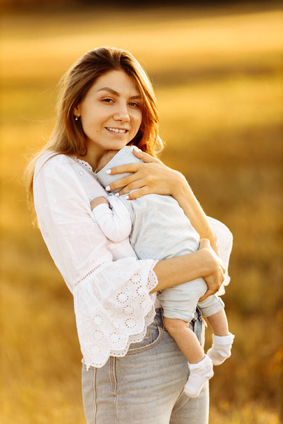 Adorable woman with beautiful newborn baby girl at the field, happy mom hold cute little daughter in arms, smiling, enjoy every moment of parenting, maternity concept   - Photo, image