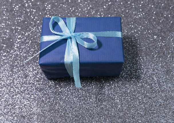 Blue box with golden ribbon on sparkling glitter paper backgound. Holiday background. Christmas concept. New year concept. - Photo, Image