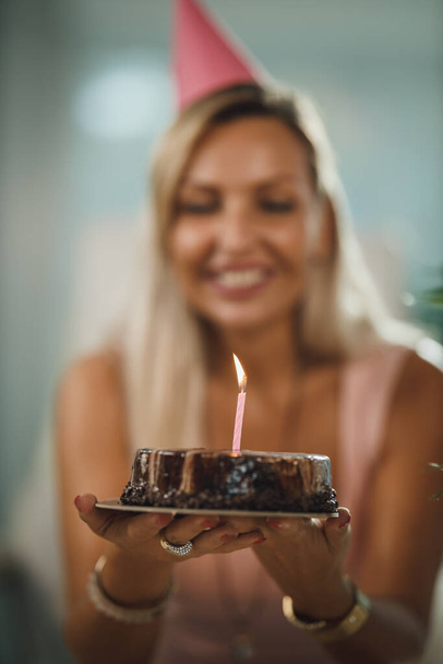 一人で魅力的な女性は、パンデミック分離中に自宅で誕生日のお祝いを持っており、友人とビデオ通話を持っています。ろうそくを灯して誕生日ケーキを持ってる. - 写真・画像