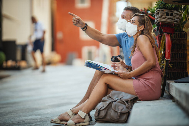 Снимок счастливой пары с защитной маской N95, проводящей время в отпуске и исследующей средиземноморский город во время пандемии короны.  - Фото, изображение