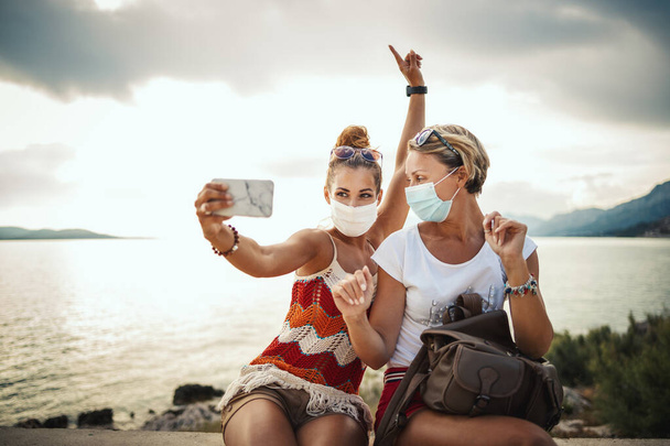 Strzał atrakcyjnych przyjaciółek w masce ochronnej i selfie ze smartfonem podczas zwiedzania wspaniałego miasta Morza Śródziemnego. - Zdjęcie, obraz