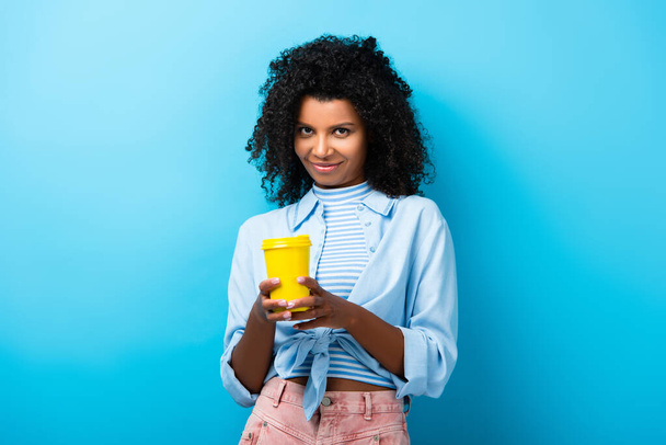 pleased african american woman holding empty reusable mug on blue - Photo, Image