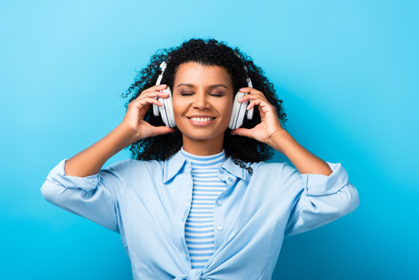 mujer afroamericana feliz escuchando música en auriculares en azul - Foto, imagen