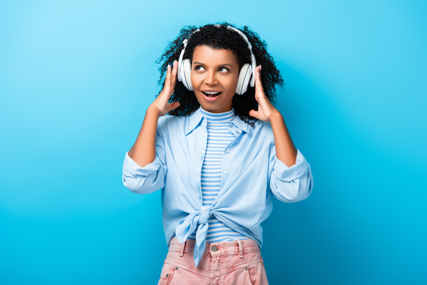 opgewonden Afrikaans amerikaanse vrouw luisteren muziek in hoofdtelefoon op blauw - Foto, afbeelding
