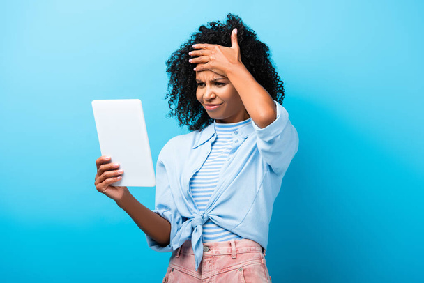 mujer afroamericana disgustado mirando tableta digital en azul  - Foto, Imagen