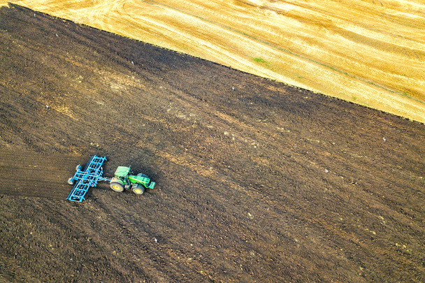 Вид с воздуха на трактор, вспахивающий черное сельскохозяйственное поле после уборки урожая поздней осенью. - Фото, изображение
