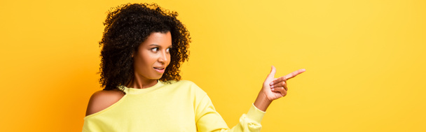 mujer afroamericana sorprendida señalando con el dedo en amarillo, bandera - Foto, imagen