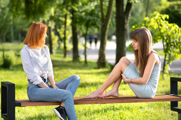 Zwei junge Freundinnen sitzen auf einer Bank im Sommerpark und unterhalten sich fröhlich. - Foto, Bild