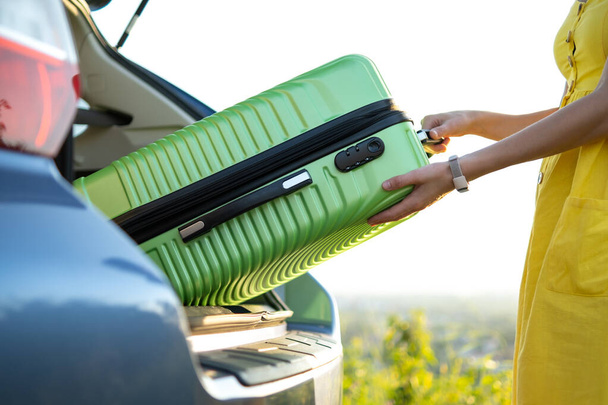 Close up of woman hands taking green suitcase from car trunk. Travel and vacations concept. - Photo, Image