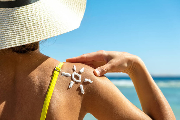 肩に太陽の形をした日焼け止めクリームでビーチで日焼け若い女性のバックビュー。紫外線日焼け対策と日焼け止めスキンケアのコンセプト - 写真・画像