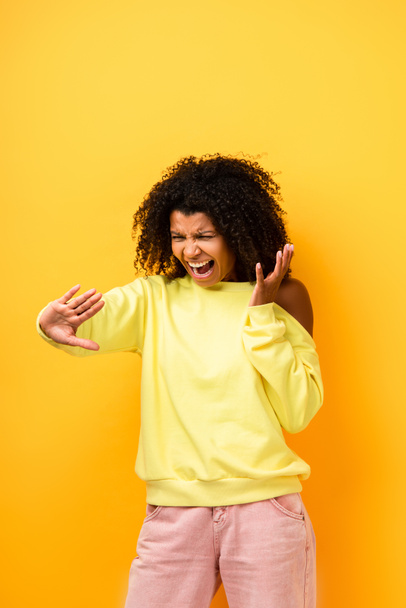 mujer afroamericana enojada mirando las uñas y gritando en amarillo - Foto, imagen