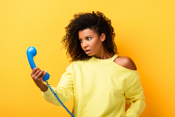 chocado Africano americano mulher olhando para vintage telefone em amarelo - Foto, Imagem