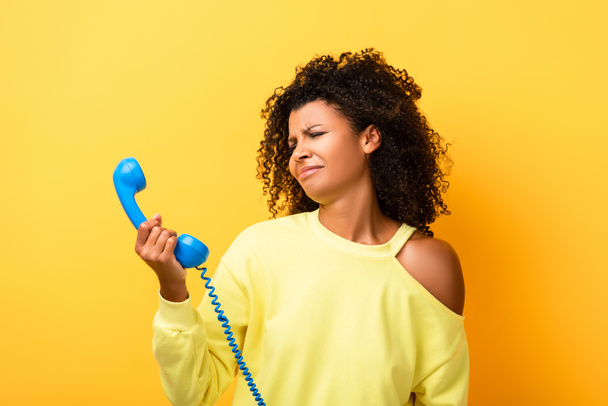 mujer afroamericana molesta mirando el teléfono vintage en amarillo - Foto, imagen