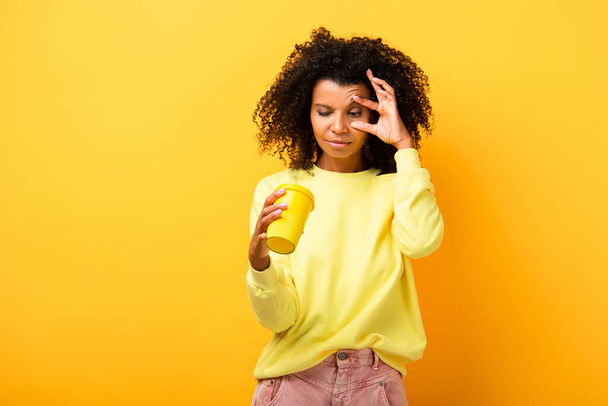 african american woman holding and looking at reusable cup on yellow - Photo, Image