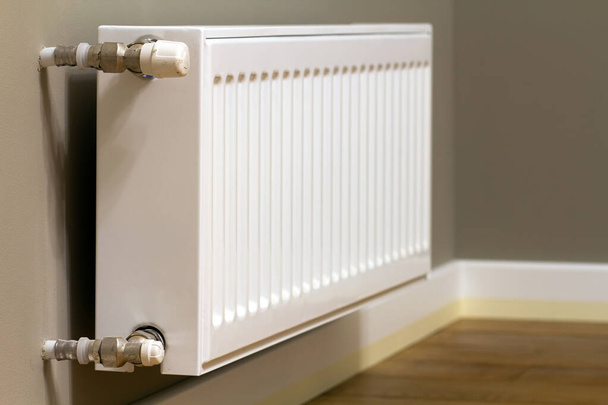 radiador de aquecimento de metal branco montado na parede cinza dentro de uma sala. - Foto, Imagem