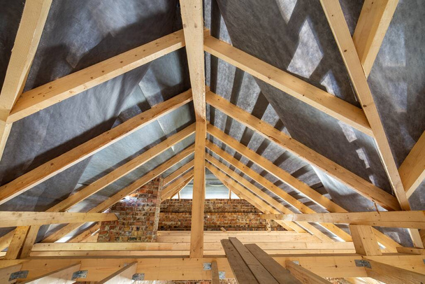Dachgeschoss eines im Bau befindlichen Gebäudes mit Holzbalken einer Dachkonstruktion und Ziegelwänden. - Foto, Bild