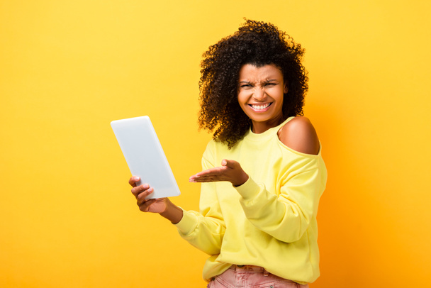 skeptical african american woman pointing with hand at digital tablet on yellow - Foto, Imagen