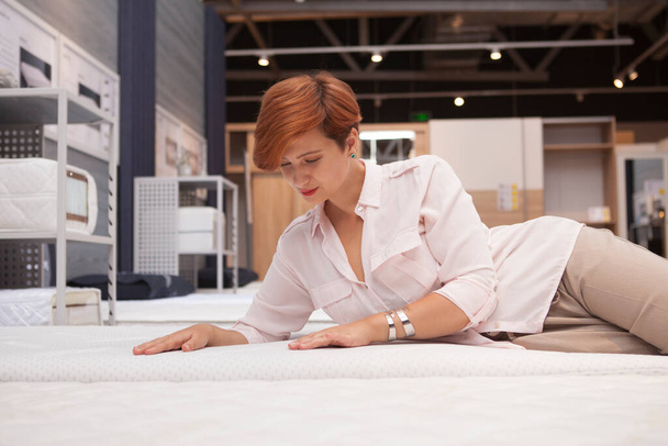 Gorgeous young woman examining orthopedic mattress, choosing new bed to buy - Photo, Image