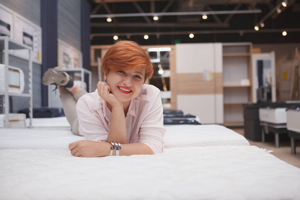Чарівна молода жінка, що розслабляється лежить на новому ортопедичному ліжку в меблевому супермаркеті, копіює простір
 - Фото, зображення