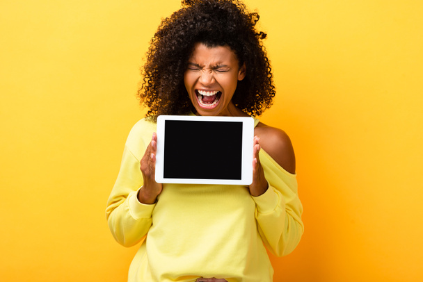 african american woman holding digital tablet with blank screen and screaming on yellow - Photo, Image