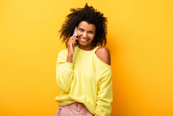 pleased african american woman talking on smartphone on yellow - Фото, зображення