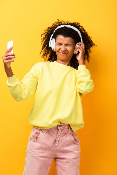 niezadowolona Afroamerykanka w słuchawkach ze smartfonem na żółto - Zdjęcie, obraz