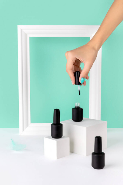 Bottle of nail varnish on podium with womans hand on turquoise background. Beauty salon product mock up template in minimal slyle. - Photo, Image