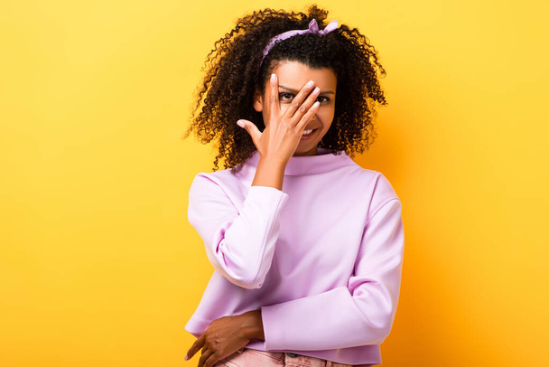 happy african american woman covering face with hand on yellow - Photo, Image