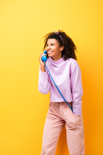 happy african american woman talking on blue retro phone on yellow - Foto, afbeelding