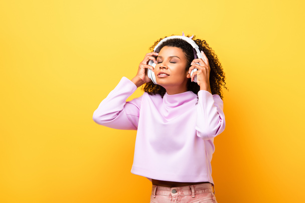 アフリカ系アメリカ人女性が黄色のワイヤレスヘッドフォンで音楽を聴き - 写真・画像