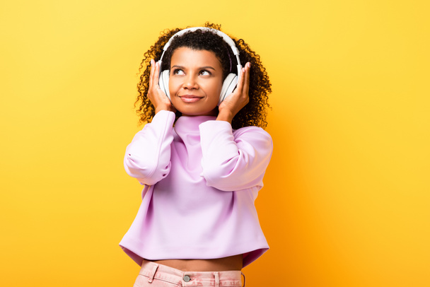 mujer afroamericana complacida escuchando música en auriculares en amarillo - Foto, imagen