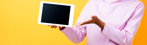 vista parcial de la mujer afroamericana apuntando con la tableta digital de la mano con la pantalla en blanco en amarillo, bandera - Foto, Imagen